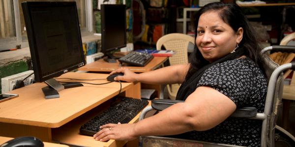 An Indian woman in a wheelchair sits at a computer desk