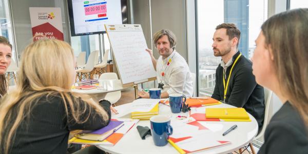Group of people sitting around a table looking at a whiteboard