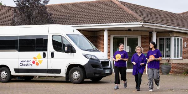 Three female care workers walking through the forecourt in front of a Leonard Cheshire branded minibus 
