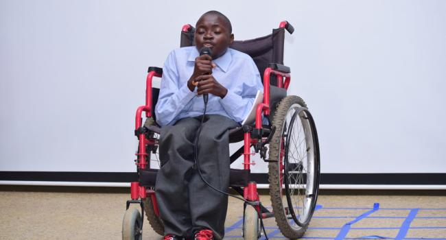Johnkeen in his wheelchair speaking into a microphone