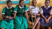 Four school girls sitting on a bench, one is wearing a leonard cheshire top with crutches in front of her