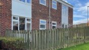 Two story flat block with white windows, a front garden and wooden fencing 