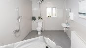 An assistive white wash bathroom with bath shower, toilet and sink 