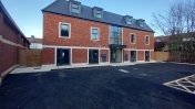 A new build red bricked building with a black tarmacked car park in front of it 