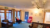 A blue carpeted lounge with brown patio windowed doors and brown sofa and chairs