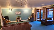 A blue carpeted lounge with one teal green wall and brown patio windowed doors and brown sofa