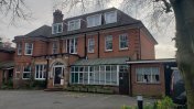 A large red bricked building with 3 floors with a car park forecourt