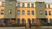 An orange and beige block of flats with 3 floors and brown panelled windows on each floor with a black gate in front of the building 