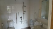 A wetroom with standing shower sink and toilet along with accessibility equipment such as pull down chair and hand rails 