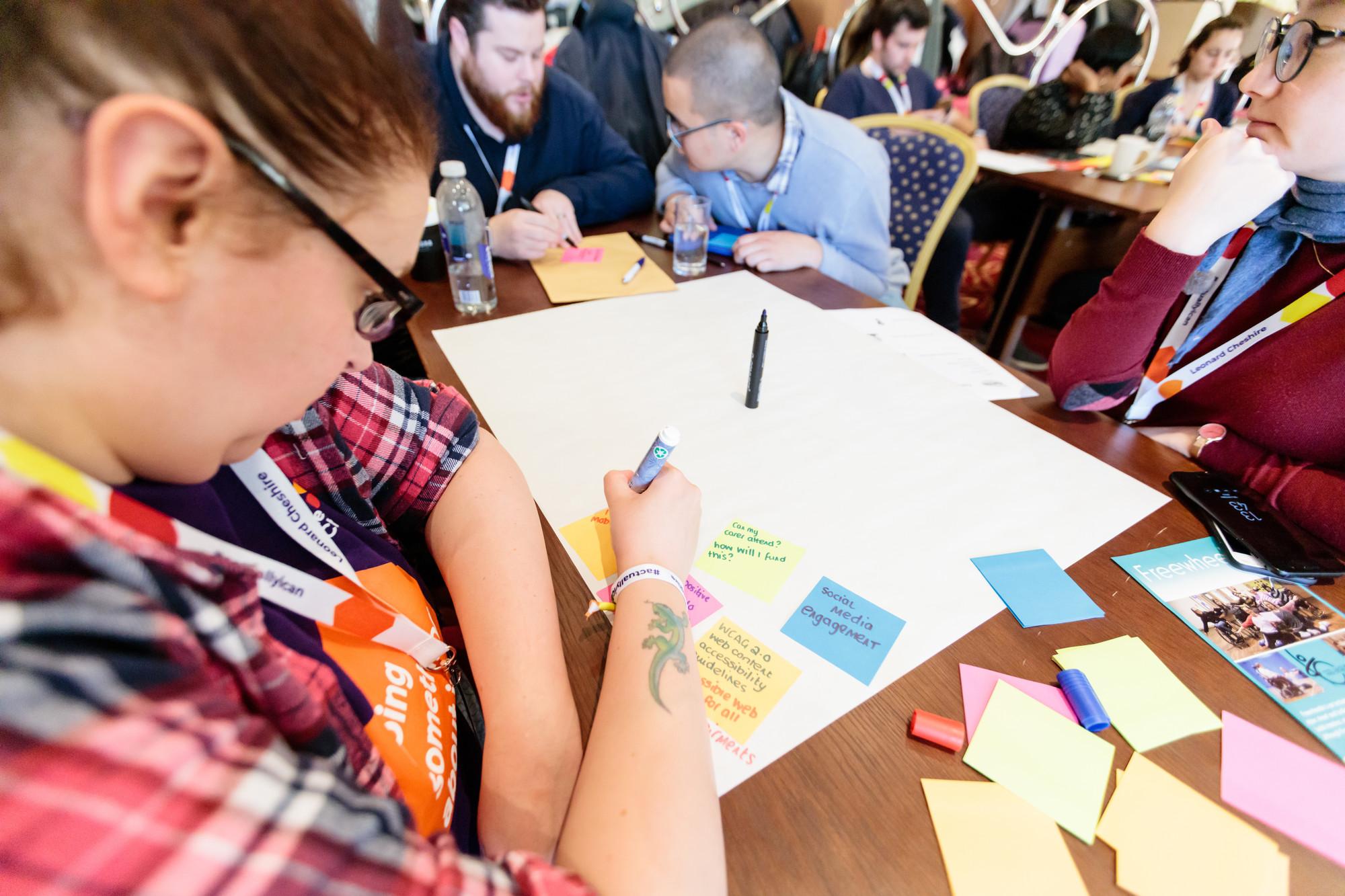 Alison, a Can Doer, sitting at a table writing on a post stick note