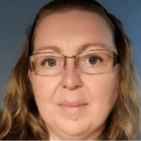 Kay a caucasian female with wavy light brown hair wearing glasses smiling at the camera