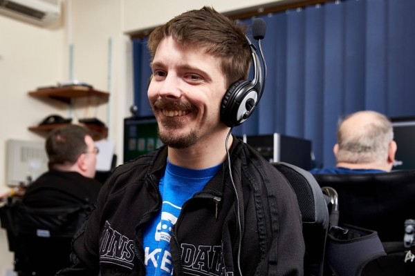 A young man wears headphones and looks at the camera while smiling