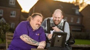 A Leonard Cheshire staff member and a resident at one of our homes watch a video on an ipad