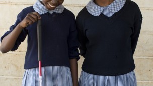 Two girls stand outside their school in blue uniforms
