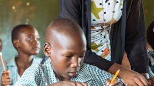 A boy writes at his desk while reading braille