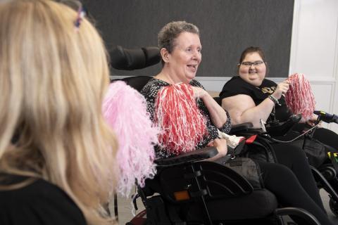 Two female wheelchair users holding red and white pom poms