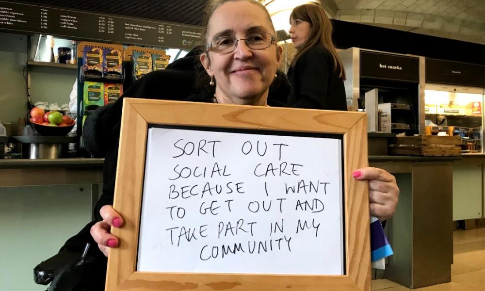 A campaigner holds a sign that reads 'Sort out social care because I want to get out and take part in my community'