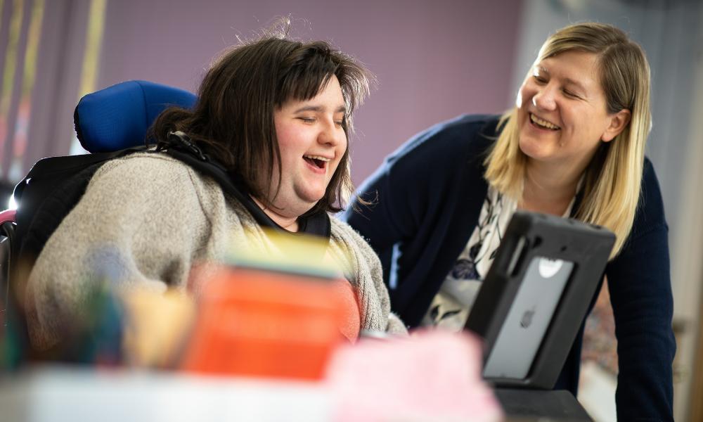 Carer and supporter laughing while looking at a tablet
