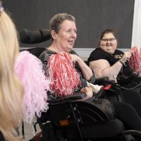 Two female wheelchair users holding red and white pom poms