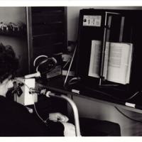 A black and white image of a Caucasian female resident using a page turner assisitive technology