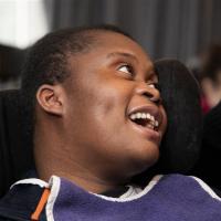 A short haired black female resident in a wheelchair smiling at someone