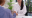 An Asian female with long dark hair and a white shirt smiling and shaking hands with a caucasian woman across a white table with a clipboard on it