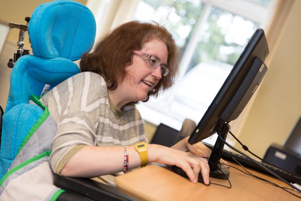 A woman who uses our services is sitting at a computer smiling