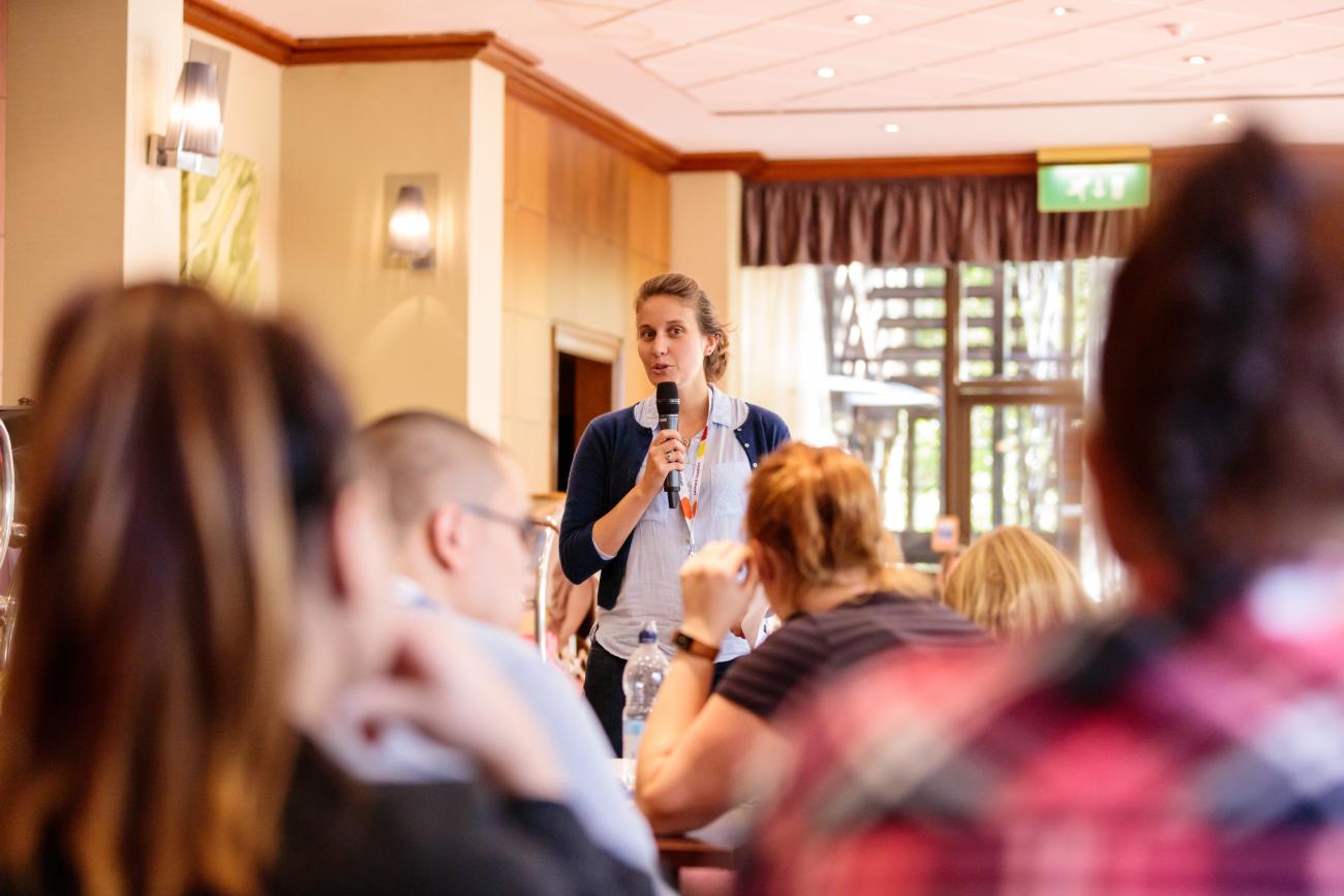 A woman talking into a microphone in front of a room full on people