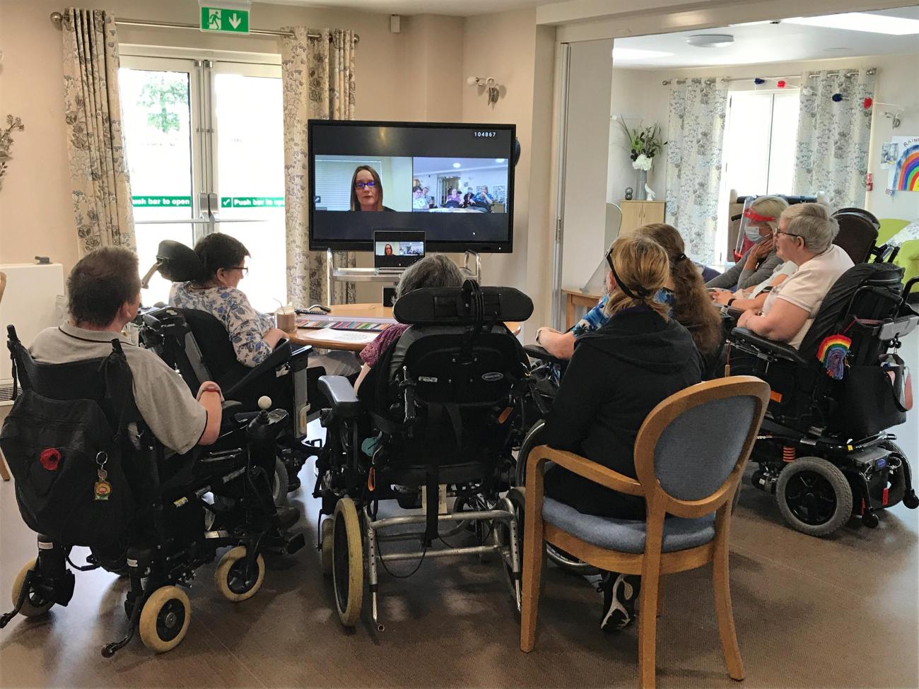 A group of people sitting around a table looking at the tv.