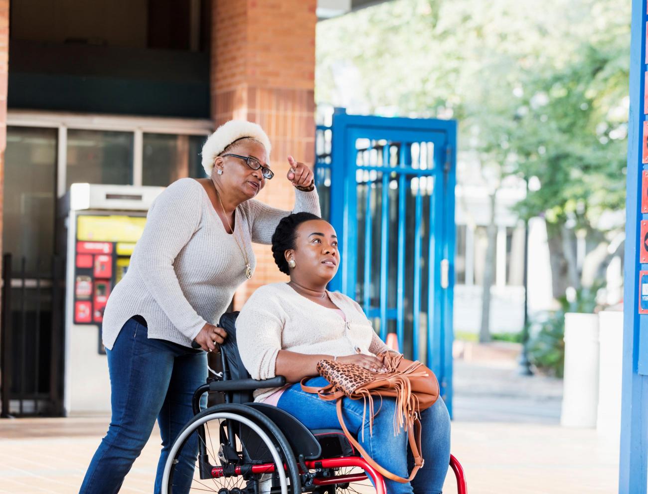 A woman in a wheelchair, being pushed by an older woman who is pointing at something