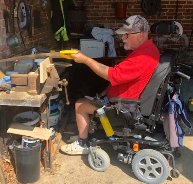 A man in his wheelchair holding a saw and cutting wood in the garden