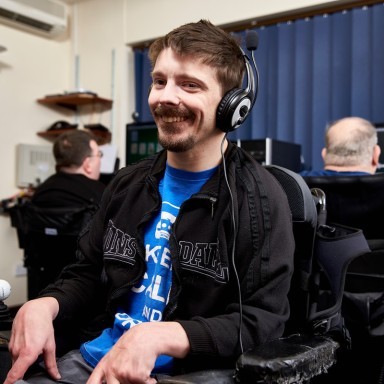 Smiling man is sitting in a computer room and wearing headphones