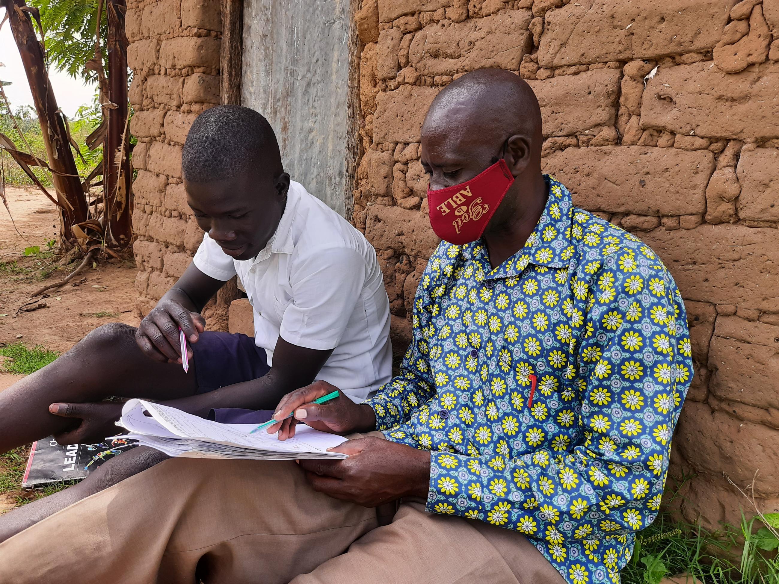 Two men sitting on the floor outside a building, they are looking a sheet of paper.