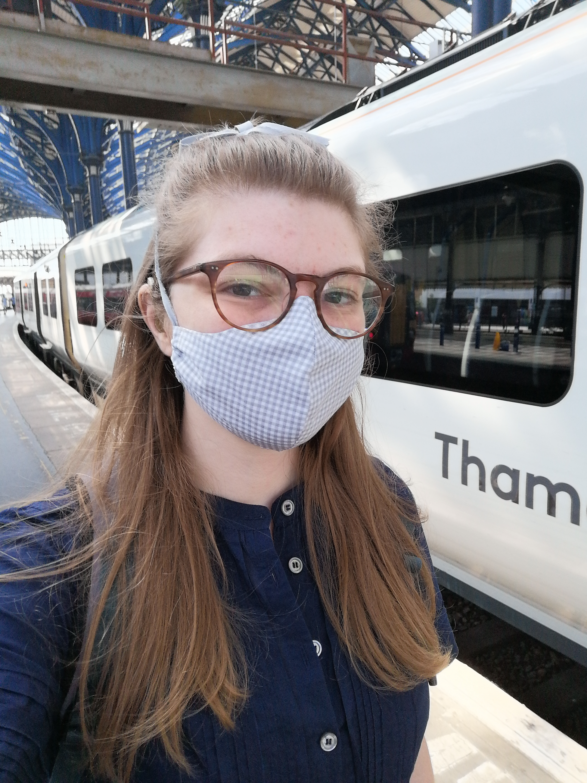 Sam wearing a face mask standing in front of a train on a platform