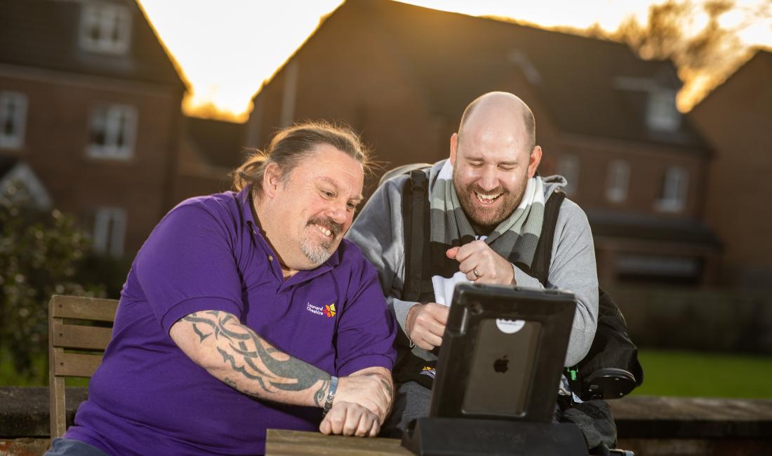 To men look at a computer screen and laugh
