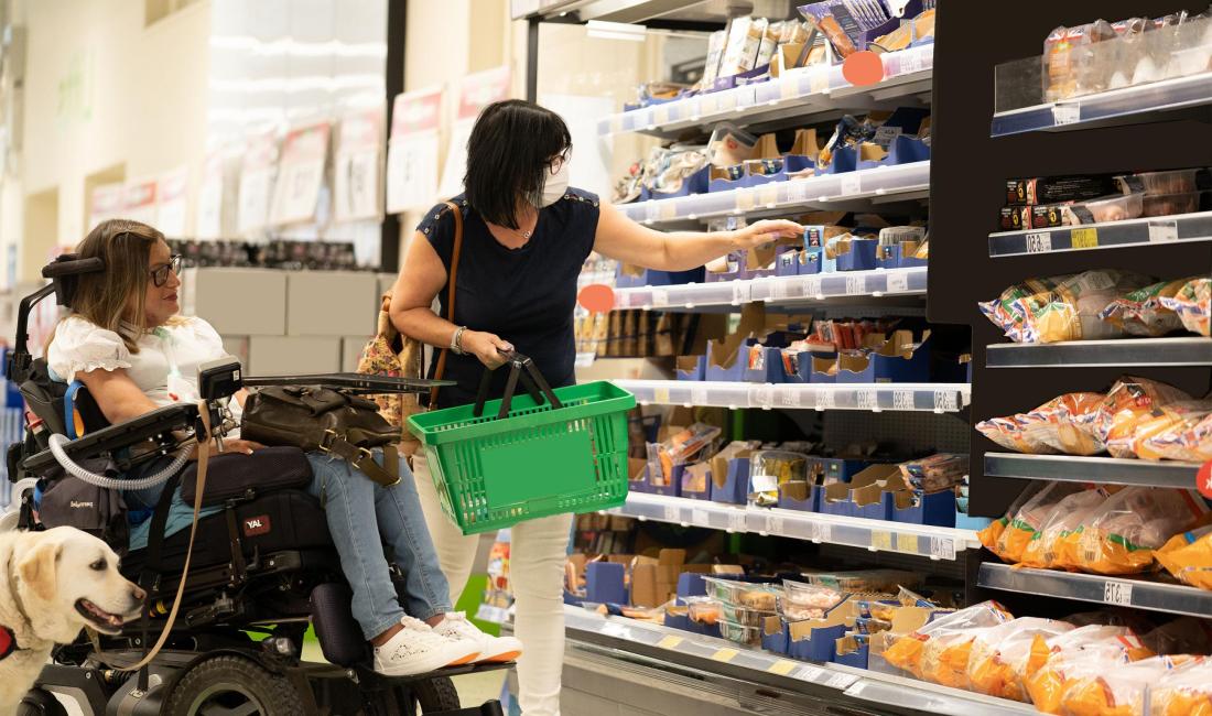 A female wheelchair user with her guide dog and carer in a supermarket
