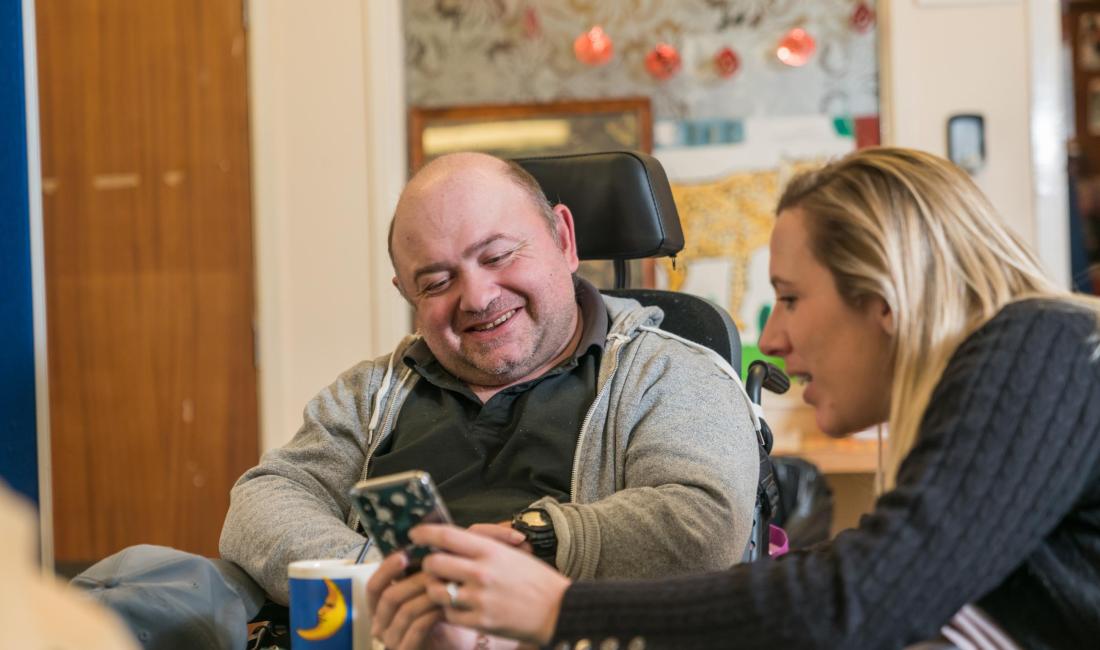 Male wheelchair user and female staff member looking at a phone